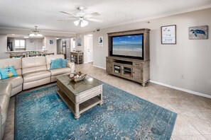 Un salon avec un canapé beige, une table basse, un téléviseur à écran plat et un tapis bleu.