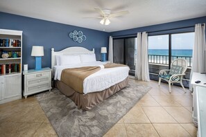 A bedroom with a bed, a nightstand, a bookshelf, a chair, and a view of the ocean.