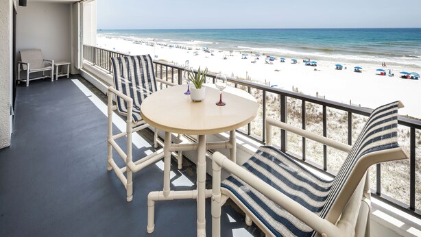 Un balcone con vista sulla spiaggia, un tavolino con una pianta e sedie a righe.