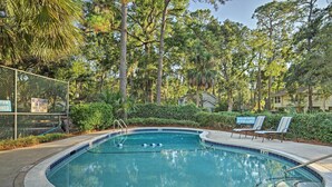 A swimming pool surrounded by trees and a fence with a lifeguard sign. - Charming Hilton Head Home on Quiet Street (Hilton Head Island)