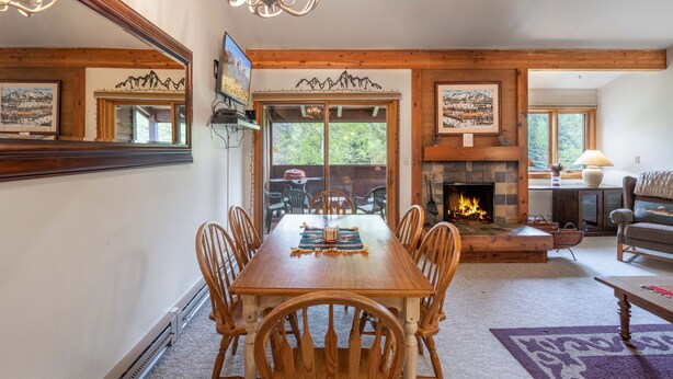Un comedor con mesa y sillas de madera, chimenea y un espejo grande que refleja la habitación.