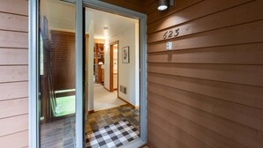 Fachada de madera con el número '623' y una puerta de cristal que da a un interior con piso a cuadros y un pasillo.