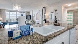 A modern kitchen with a granite countertop, white sink, and stainless steel faucet. There are toiletries on the counter, and a large window provides a view of the outdoors. - Island Princess 609 * Gulf front~Beach Chair Set Included * Salt Water Vacations (Fort Walton Beach)
