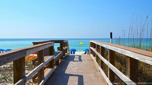 A wooden boardwalk leading to a beach with umbrellas and a flag. - Island Princess 609 * Gulf front~Beach Chair Set Included * Salt Water Vacations (Fort Walton Beach)