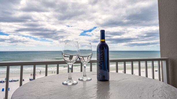 A table with two empty wine glasses and a bottle on a balcony overlooking a beach. - Island Princess 609 * Gulf front~Beach Chair Set Included * Salt Water Vacations (Fort Walton Beach)