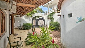 A courtyard with a tiled floor, a wooden pergola, a bench, and potted plants.