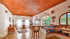 A spacious living area with a tiled floor, a wooden ceiling, and a kitchen with a bar counter.