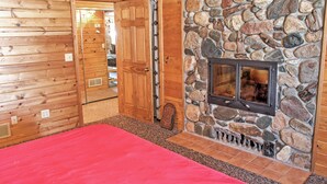 A log cabin interior with a stone fireplace, wooden walls, and a red carpet. - Wonderful Home on Sand Lake w/ Expansive Porch! (Spring Lake)