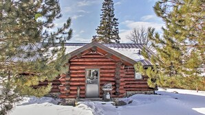 A log cabin with a metal roof, surrounded by snow and pine trees. - Wonderful Home on Sand Lake w/ Expansive Porch! (Spring Lake)