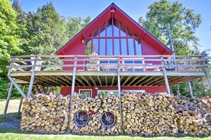 Ein rotes Bauernhaus mit einer Holzterrasse und einem Holzstapel davor.
