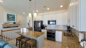 Una cocina moderna con armarios blancos, encimeras de granito, horno empotrado, microondas y una isla grande con taburetes de bar.