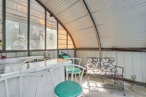 A covered outdoor seating area with a table and chairs, a water fountain, and a view of the surrounding trees.
