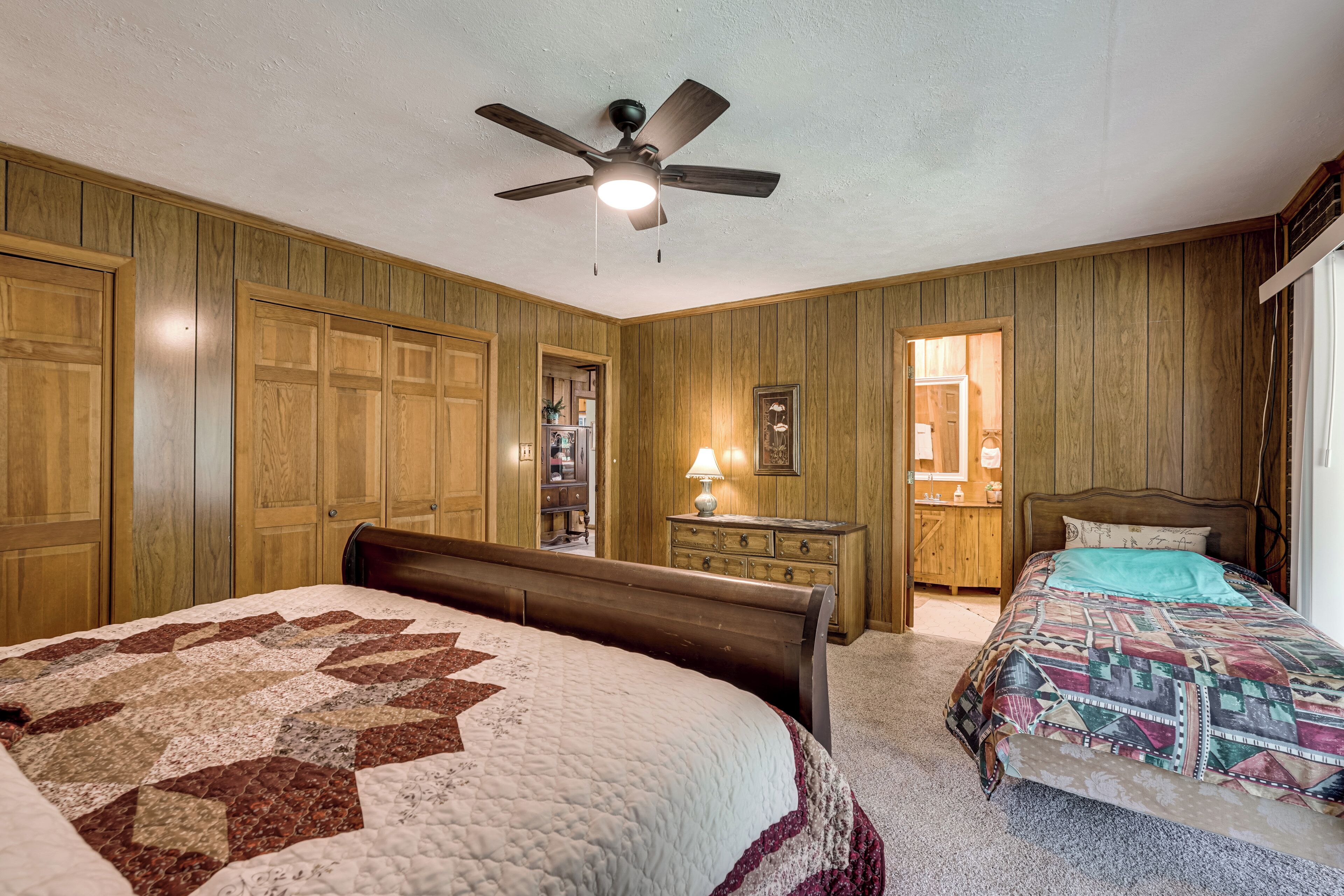 A bedroom with two beds, wooden paneling, a ceiling fan, and a dresser.