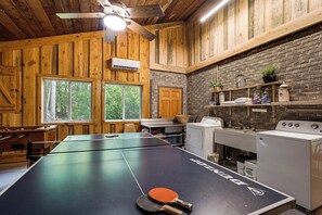 Un interior de madera con mesa de ping pong, ventilador de techo y pared de ladrillo.