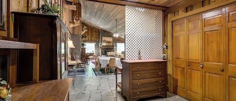 A rustic interior with a stone floor, wooden walls, a dining area, and a fireplace.