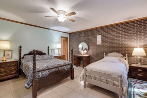 A bedroom with two beds, a ceiling fan, a brick wall, and a wooden dresser.