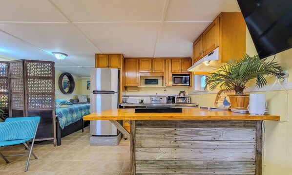 A compact kitchen with wooden cabinets, a refrigerator, a microwave, and a sink.