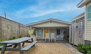 A small, single-story building with a covered patio area, a wooden fence, and a sign indicating a vacation rental.