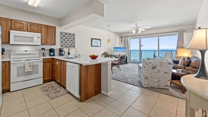 A modern kitchen with wooden cabinets, a white microwave, and a large island. There is a dining area with a view of the ocean.
