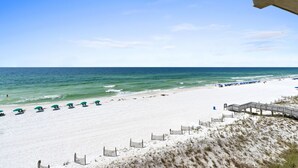 A beach with white sand, a wooden boardwalk, and green umbrellas.