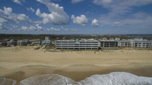 Ein Strandhotel mit mehreren Gebäuden, einem Sandstrand und brechenden Wellen.