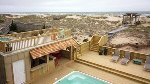 A wooden deck with a pool, outdoor seating, and a view of the beach.