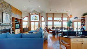 A spacious living area with a large blue sofa, wooden cabinets, a stone fireplace, and a view of the beach through large windows.