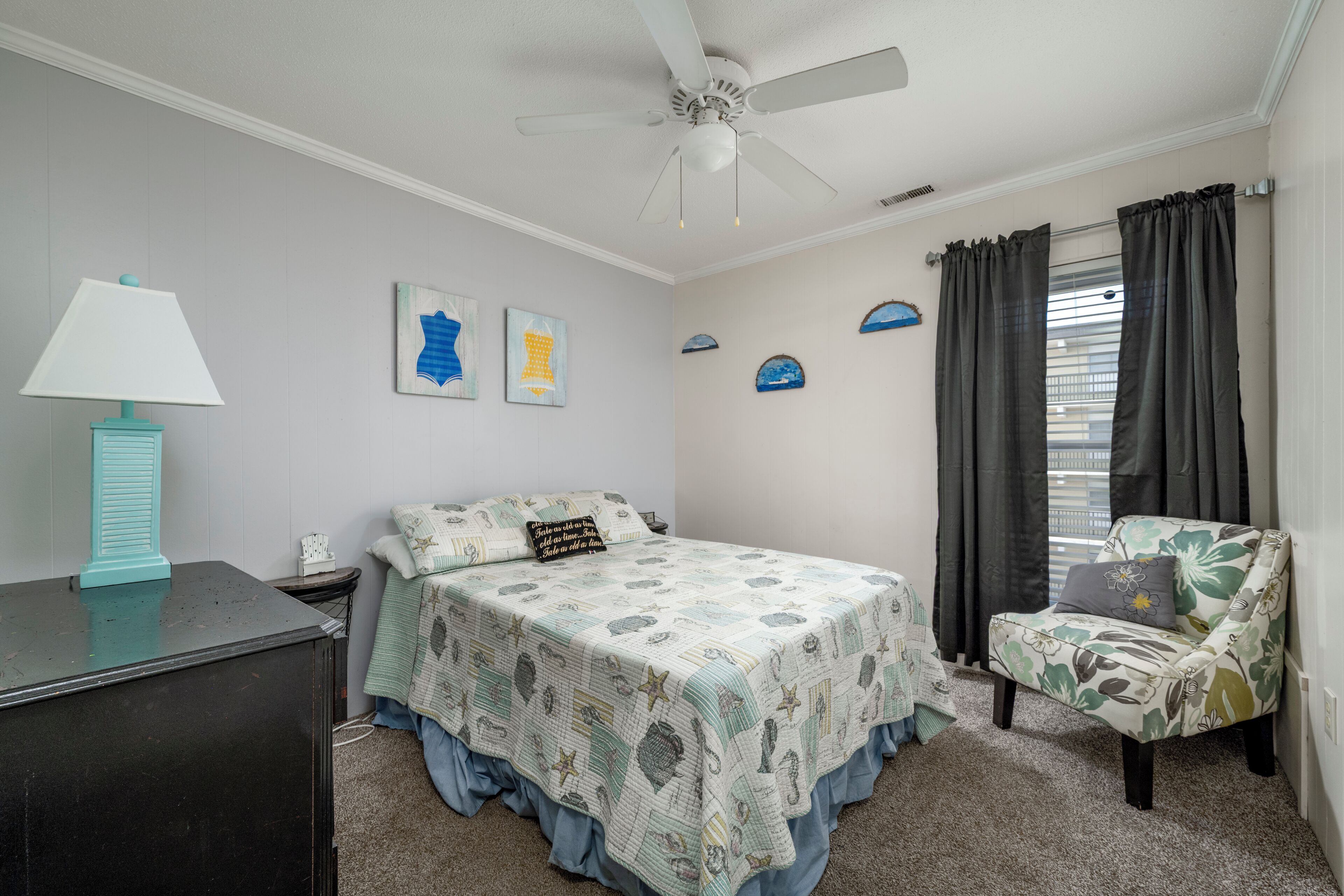Ein Schlafzimmer mit Bett, Stuhl, Schreibtisch, Lampe und Deckenventilator.