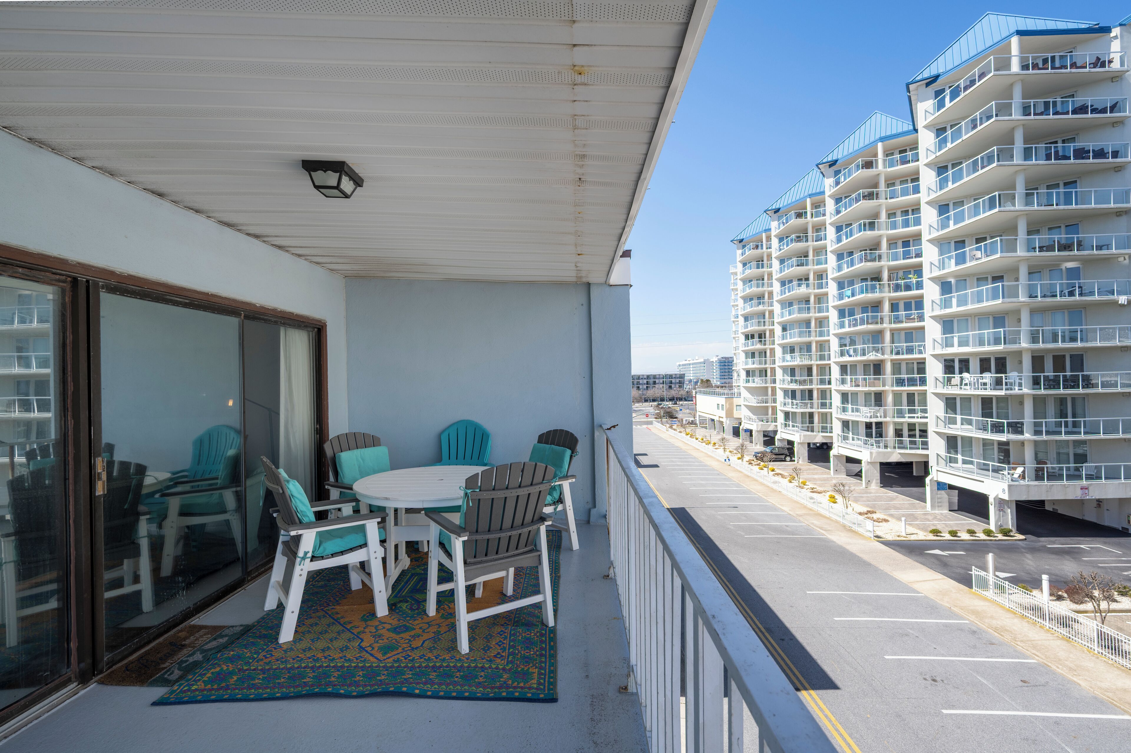 A balcony with a table and chairs, a patterned rug, and a view of a multi-story building with balconies.