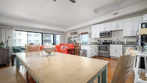Una cocina moderna con armarios blancos, un microondas y una estufa. Hay un comedor con una mesa y sillas de madera.