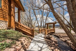 Une cabane en bois avec des fondations en pierre, une véranda en bois et un chemin de pierre menant à un belvédère.