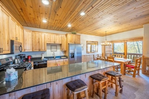 Une cuisine spacieuse avec des meubles en bois, un grand îlot central doté de tabourets et une vue sur l’extérieur grâce à de grandes fenêtres.