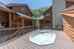 Une cabane en bois avec un jacuzzi sur une terrasse, des murs en pierre et un porche abrité.