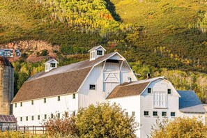 A white barn with a gabled roof and a large door, surrounded by trees and a hill in the background. - Three Kings 1 at Park City Mountain (Park City)