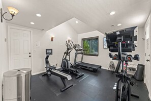 A home gym with exercise equipment, a door, a trash can, and a window with blinds.