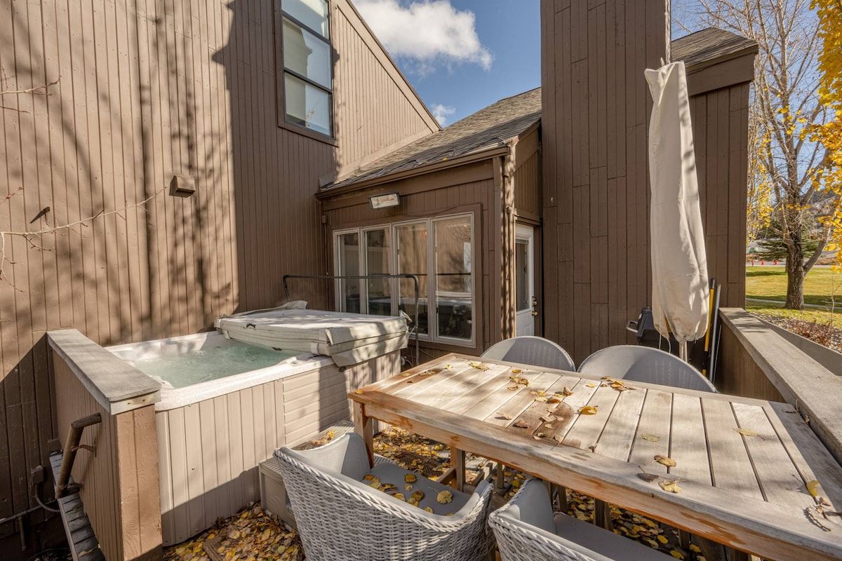 A wooden deck with a hot tub, a table, and chairs.