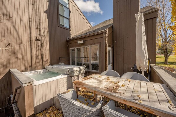A wooden deck with a hot tub, a table, and chairs.