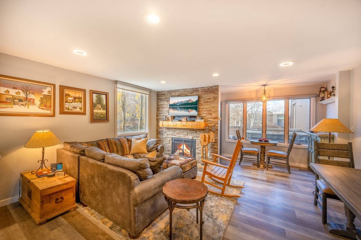 A cozy living room with a fireplace, comfortable seating, and a view of the outdoors.
