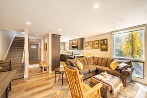 A spacious living area with a sofa, coffee table, and wooden furniture. A kitchen is visible in the background with modern appliances. - Three Kings 1 at Park City Mountain (Park City)