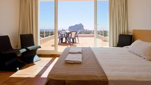 A hotel room with a bed, a small table with chairs, and a view of a cityscape through large windows.