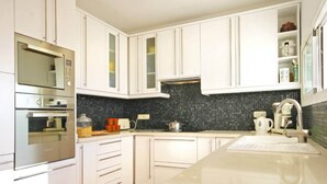 A modern kitchen with white cabinetry, a black backsplash, and stainless steel appliances.