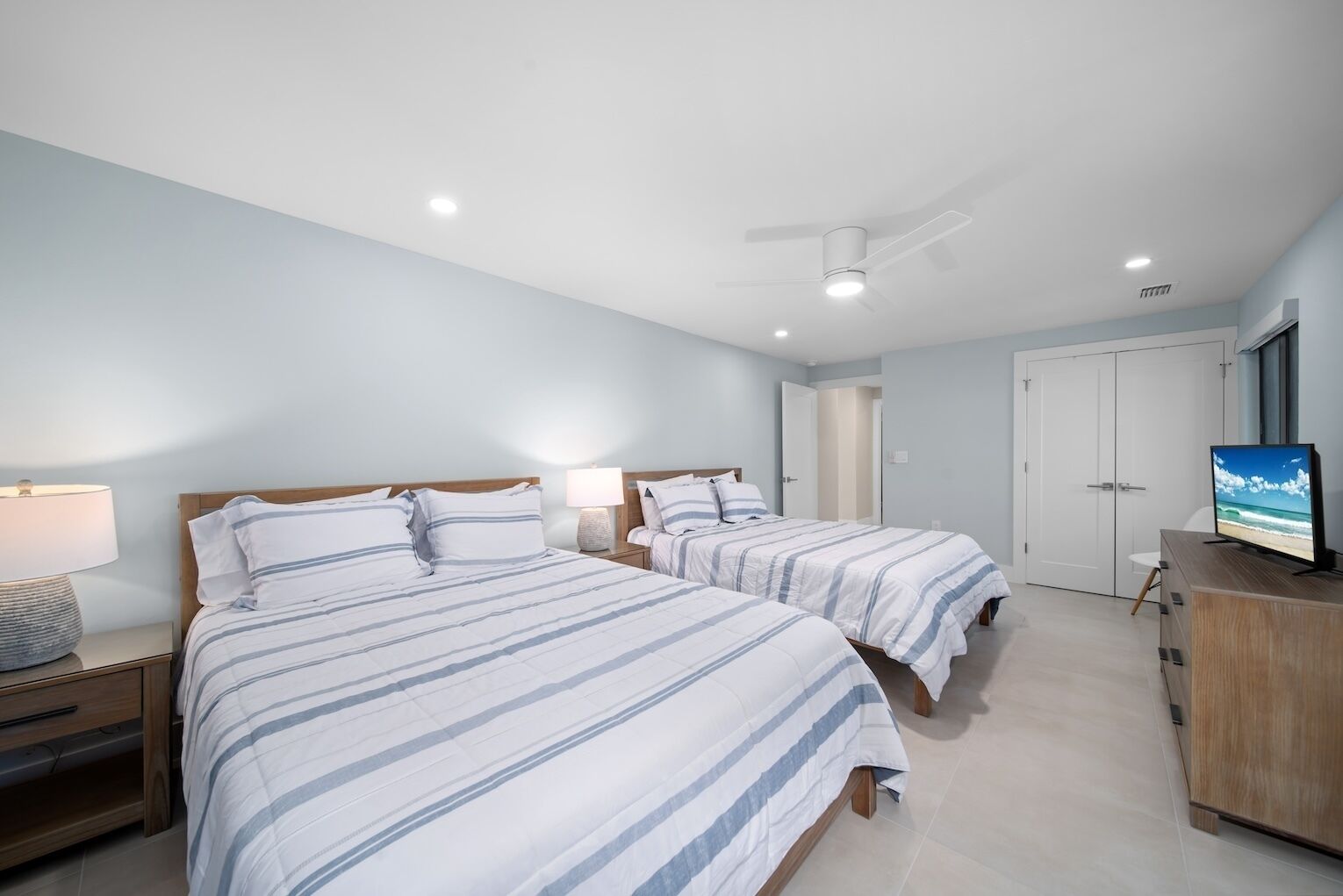 A hotel room with two beds, a TV, a ceiling fan, and a door leading to a bathroom.