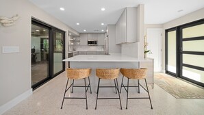 Una cucina moderna con isola centrale, tre sedie di vimini e vista sull'adiacente sala da pranzo.