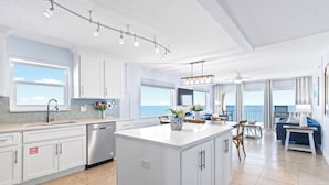 Une cuisine moderne dotée d’un grand îlot central, de meubles blancs et offrant une vue sur l’océan.