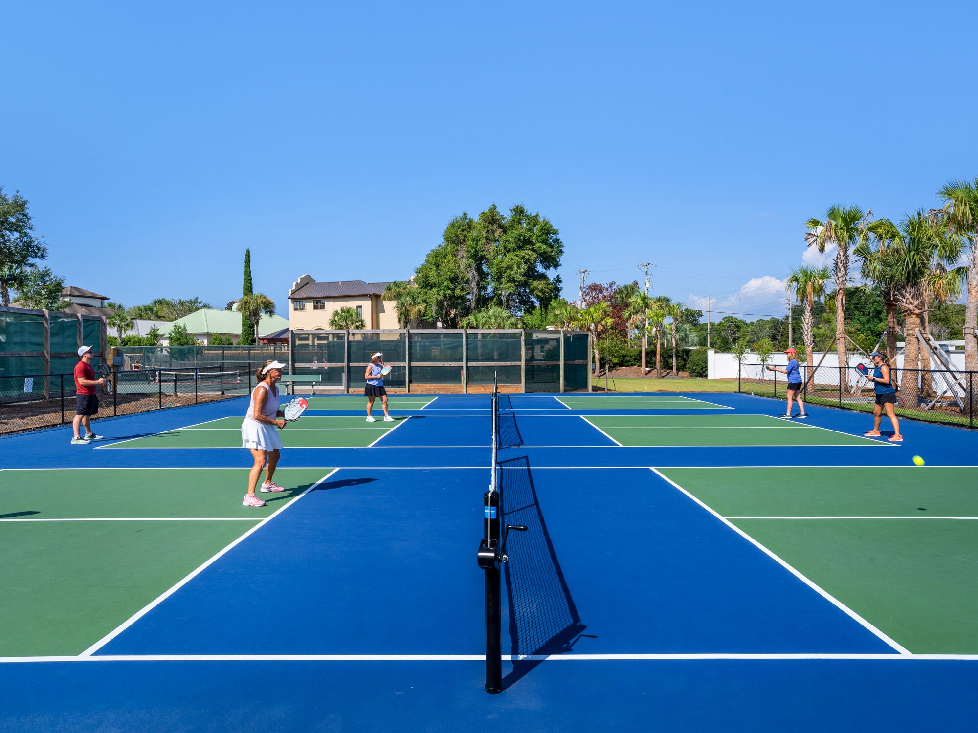 Un court de tennis avec plusieurs joueurs, un filet et une maison en arrière-plan.
