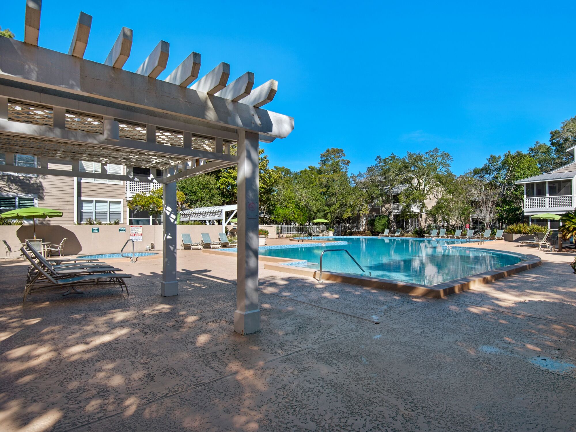 Ein Poolbereich mit Liegestühlen, einer Pergola und blauem Himmel.