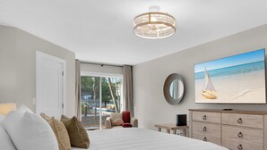 Ein Hotelzimmer mit einem großen Bett, einem Fernseher, einer Holzkommode und Blick auf den Strand.
