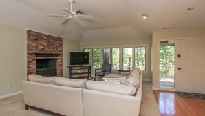 A living room with a brick fireplace, a beige sectional sofa, a television, and a ceiling fan. - 1 Deer Run: Newly Listed & Furnished Home, Dog Friendly, 4 BR, Bikes (Hilton Head Island)