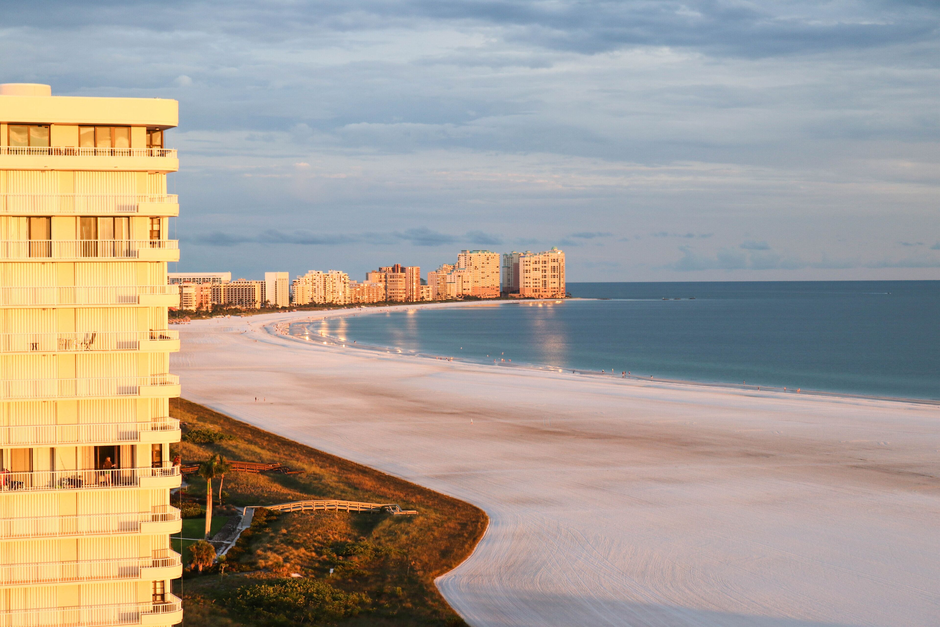 A beachfront hotel with multiple floors, a curved shoreline, and a view of the ocean.