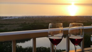 Two glasses of red wine on a balcony with a sunset view over a body of water. - Great Beach Views, Direct Access, Pickleball, New Kitchen & Heated Pool! Tower 3 (Marco Island)